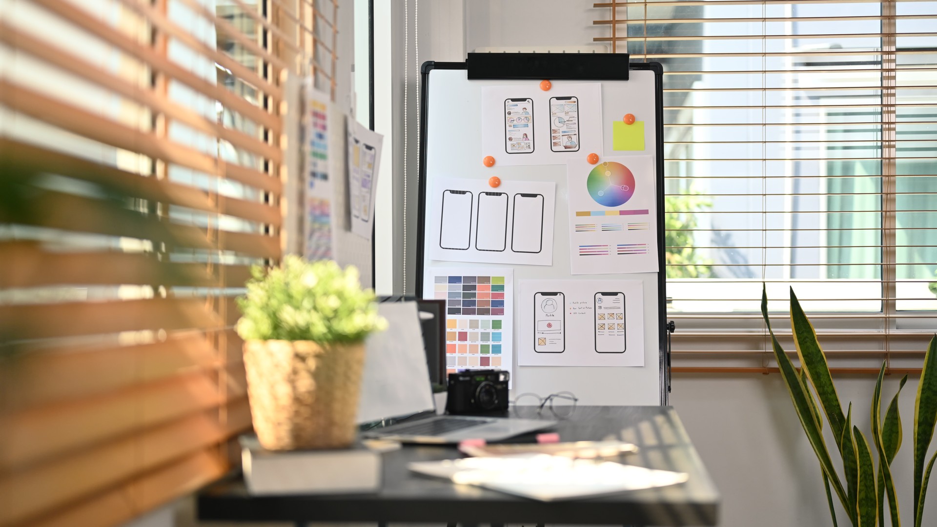 Creative office with laptop, stationery and wireframe sketches of screens for mobile application on a flip board.